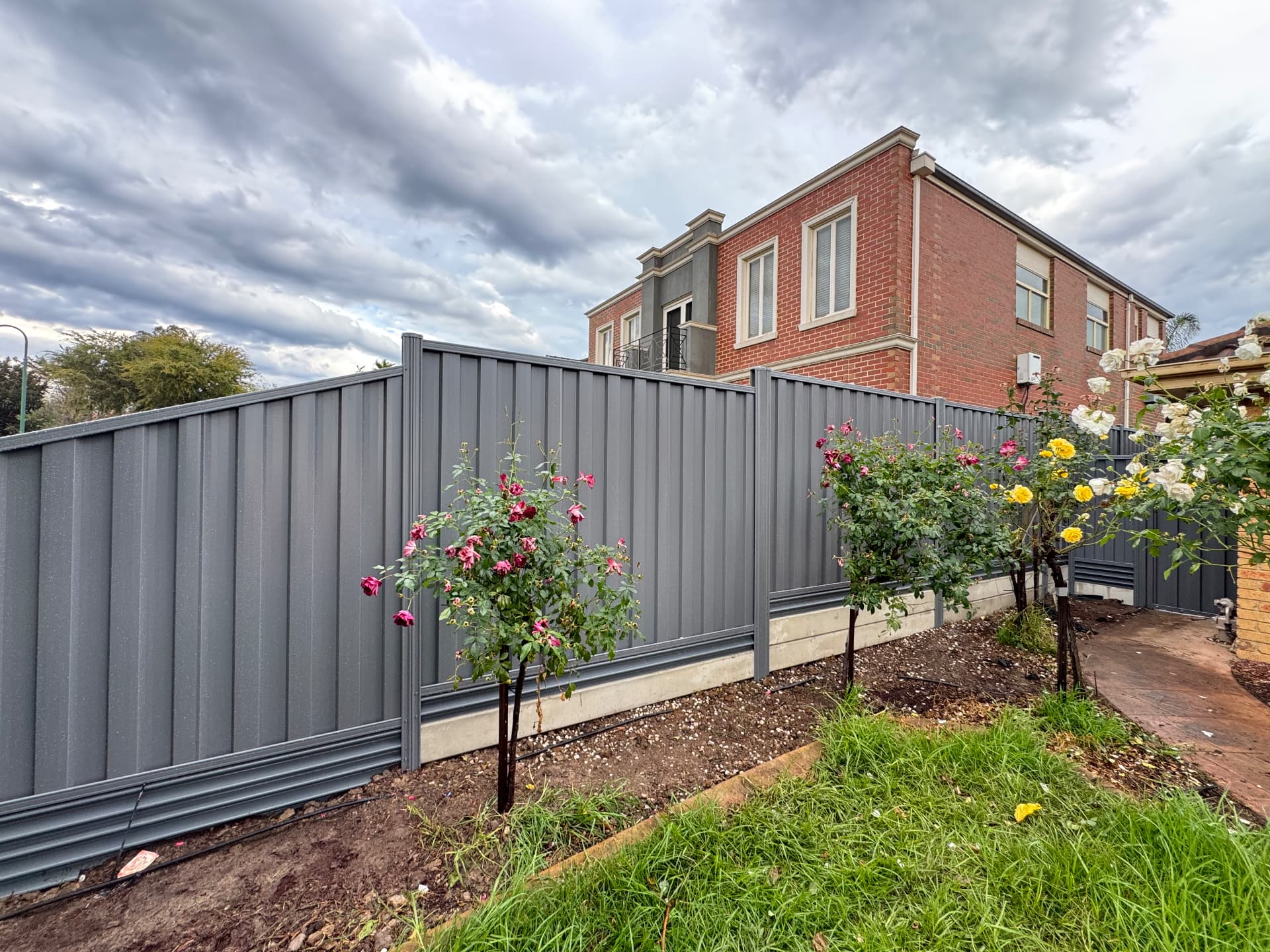 Grey Colorbond boundary fence on concrete plinths with garden bed