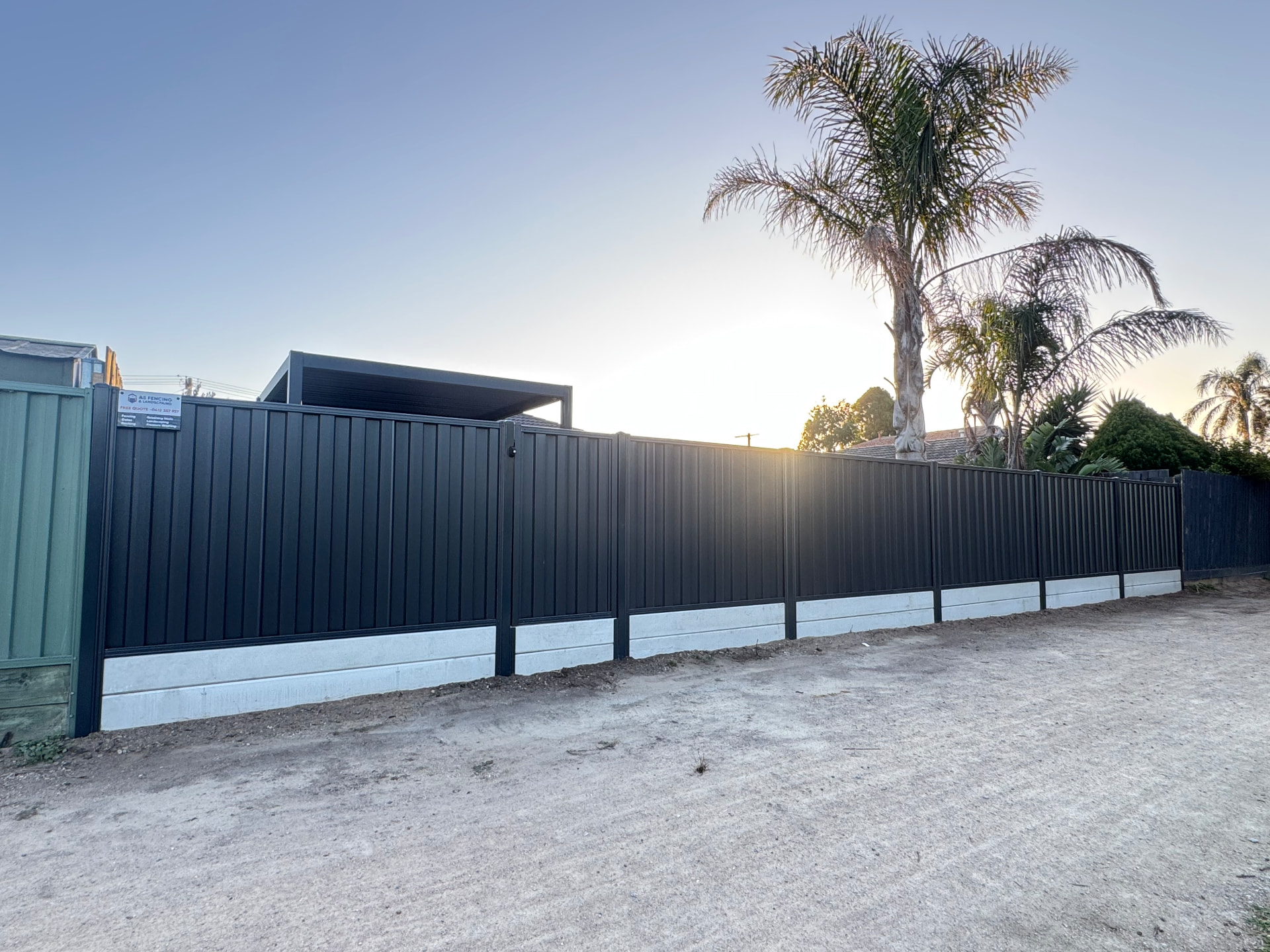 Long charcoal Colorbond boundary fence with concrete sleeper plinths at sunset