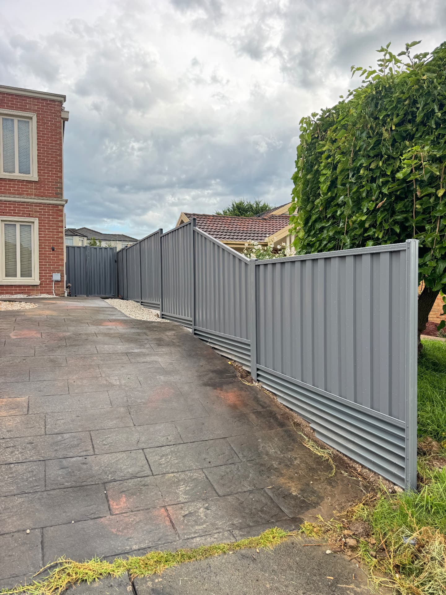 Stepped grey Colorbond fence and matching gate beside a paved driveway